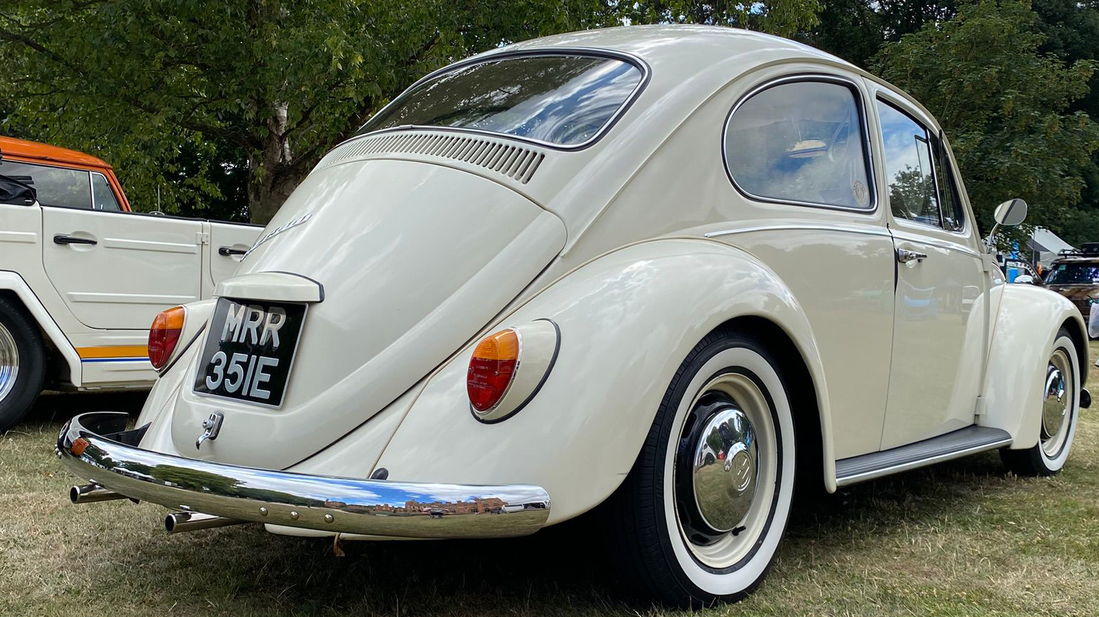 Rear right view of a cream classic Volkswagen Beetle wedding car with chrome detailing and whitewall tyres