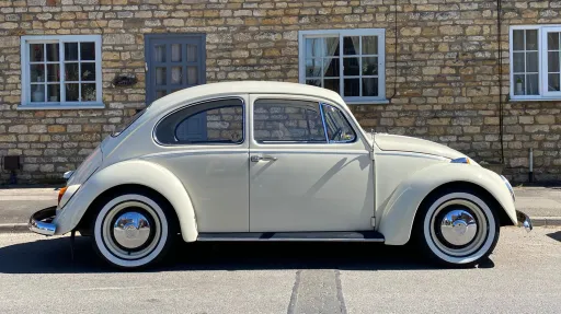 Right side profile of a cream classic Volkswagen Beetle wedding car parked beside a stone building