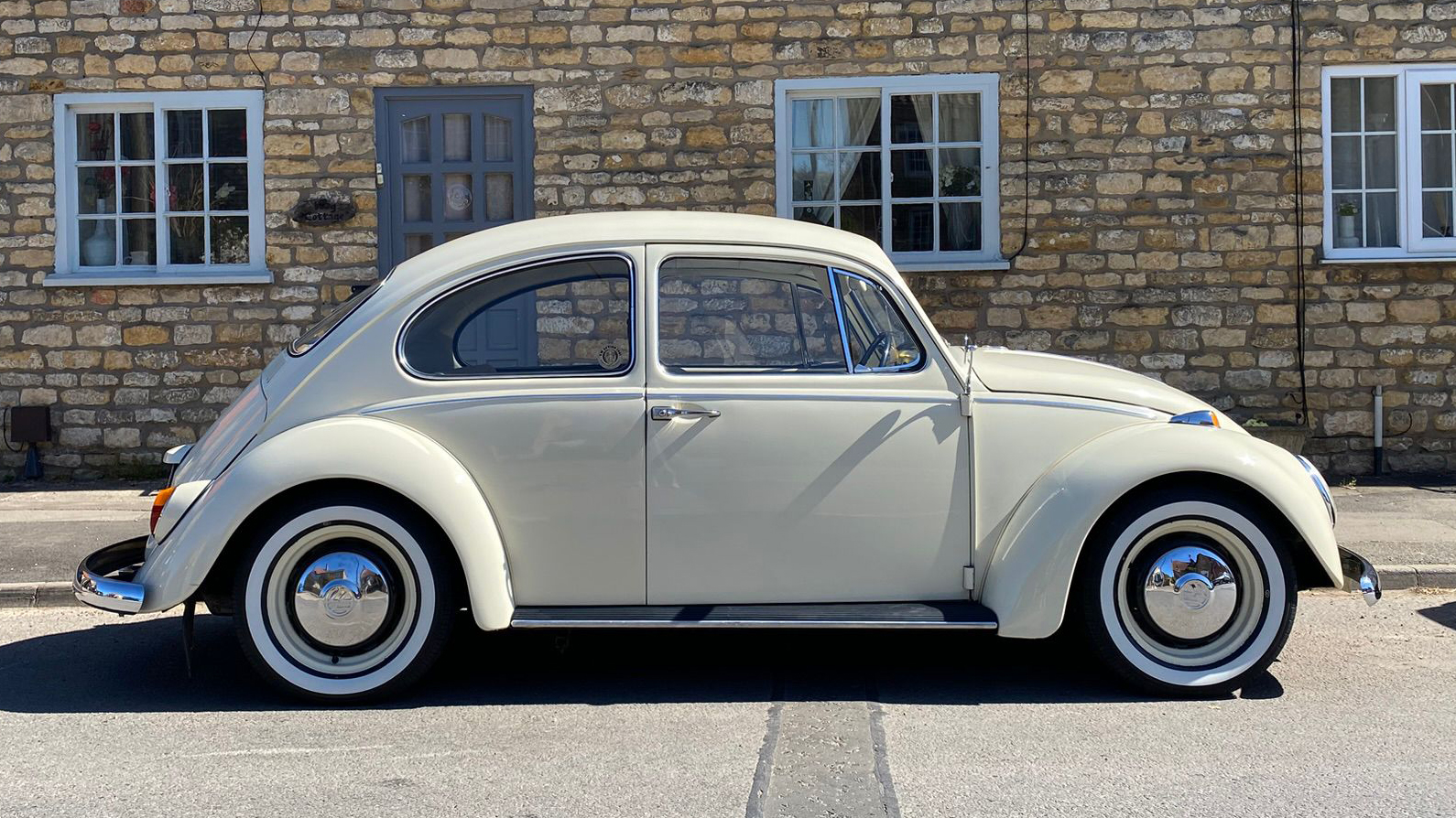 Right side profile of a cream classic Volkswagen Beetle wedding car parked beside a stone building