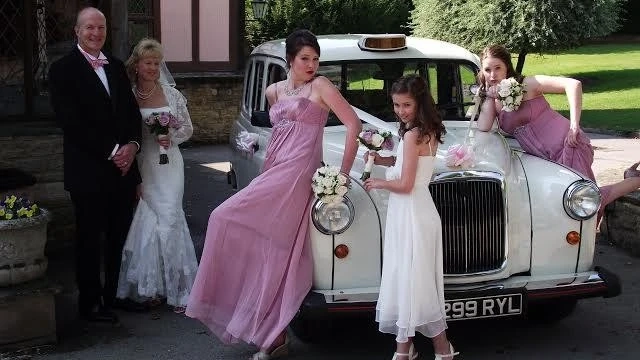 Wedding guests gathered around an ivory and cream classic London taxi decorated with ribbons and flowers.