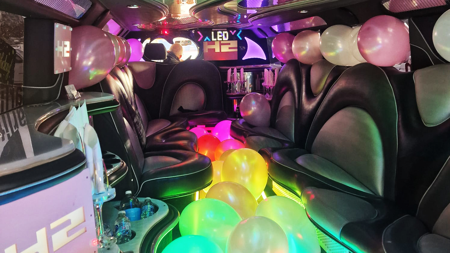 Interior of 16 seater Hummer limousine with black leather seats, LED lighting, balloons and illuminated floor.