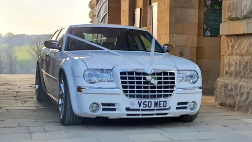 White Chrysler 300C wedding car parked outside venue with traditional white ribbons