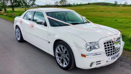 Side profile of white Chrysler 300C saloon dressed with wedding ribbons and chrome wheels