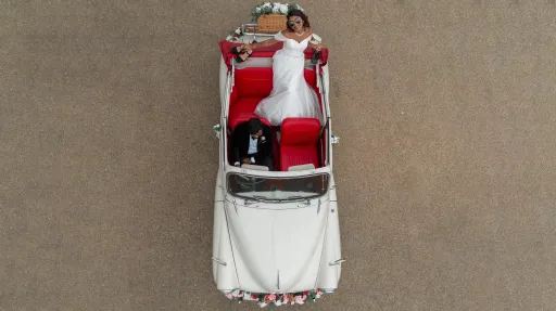 Aerial view of cream 1963 Morris Minor Convertible showing contrasting red leather interior. Groom seatingh in the Driver's seat while Bride is eating in the rear in a white wedding gown.