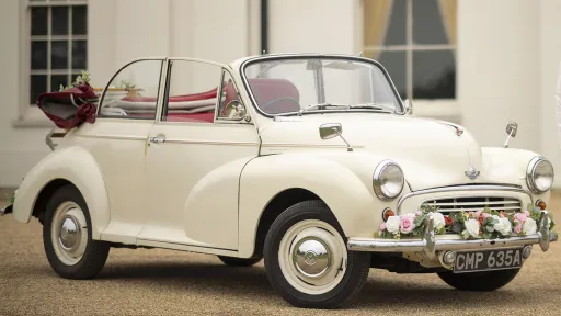 1963 Morris Minor Convertible in cream parked outside a grand wedding venue, hood down with red leather interior visible.
