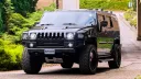 Black Hummer H2 parked on a country road near a wedding venue with greenery and trees in the background.