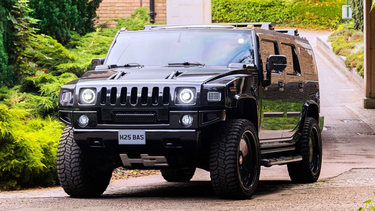 Black Hummer H2 parked on a country road near a wedding venue with greenery and trees in the background.