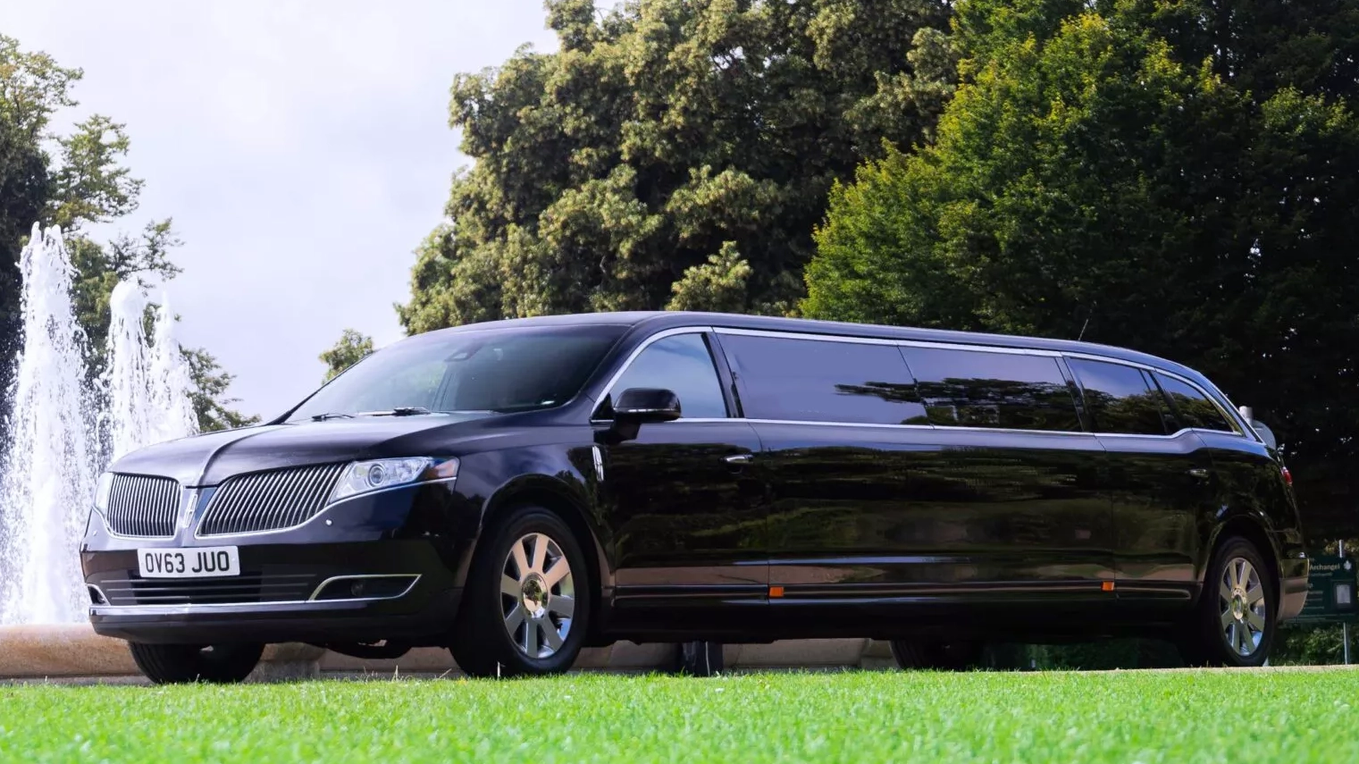 Black Lincoln MKT stretch limousine parked on grass near a fountain with tinted windows and extended body styling.