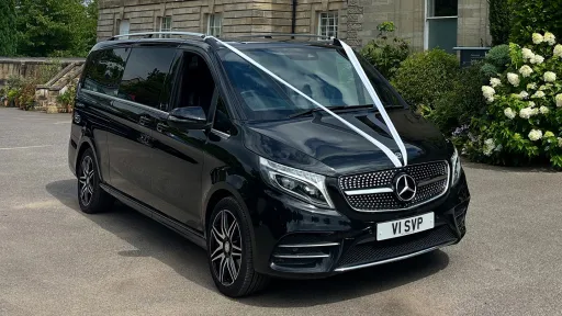Black Mercedes V-Class multi-seater parked outside venue, dressed with white V-shape ribbon.
