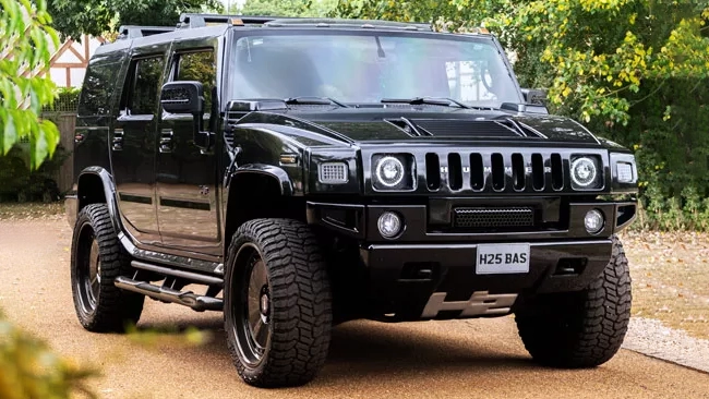 Front view of black Hummer H2 with bold grille and headlights parked outdoors on gravel.
