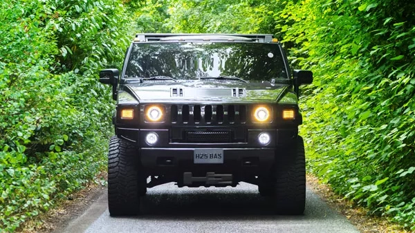 Front view of black Hummer H2 driving along a narrow country road surrounded by green hedges.