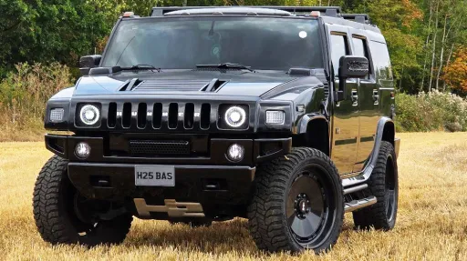 Front three quarter view of black Hummer H2 SUV parked on a driveway with trees behind.