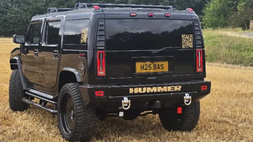 Rear view of black Hummer H2 parked in a field showing vertical tail lights and wide stance.