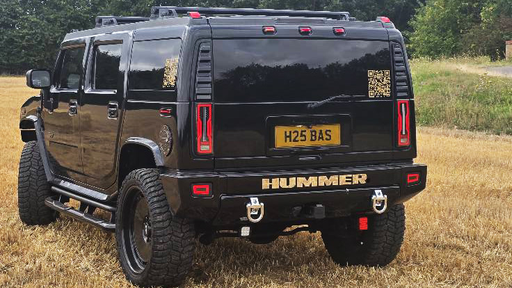 Rear view of black Hummer H2 parked in a field showing vertical tail lights and wide stance.