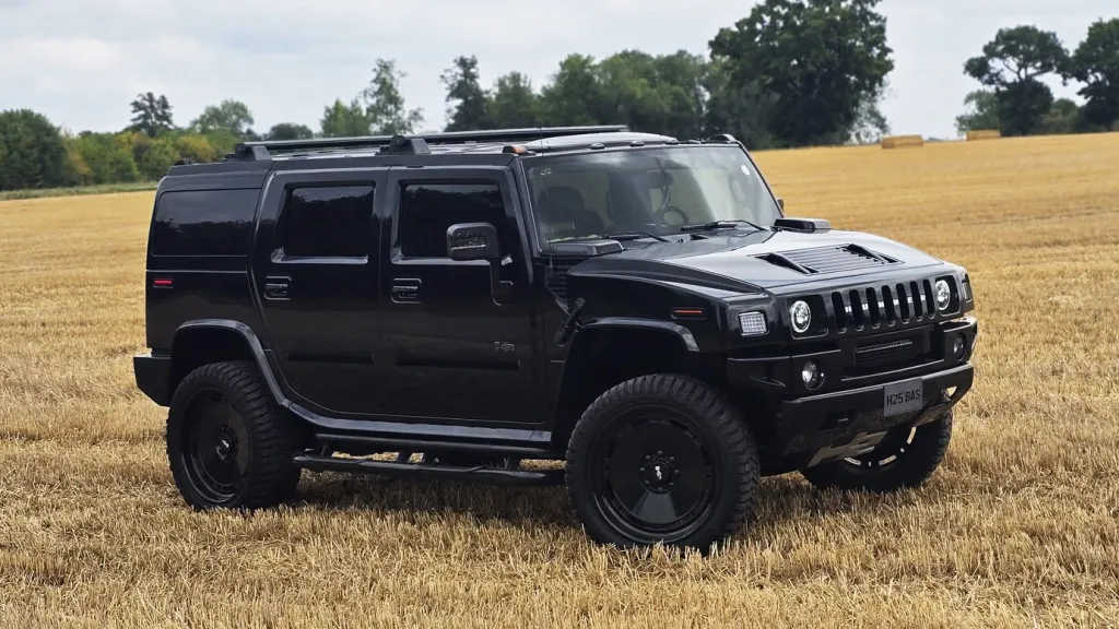 Right side view of black Hummer H2 with privacy tinted windows parked in an open field.