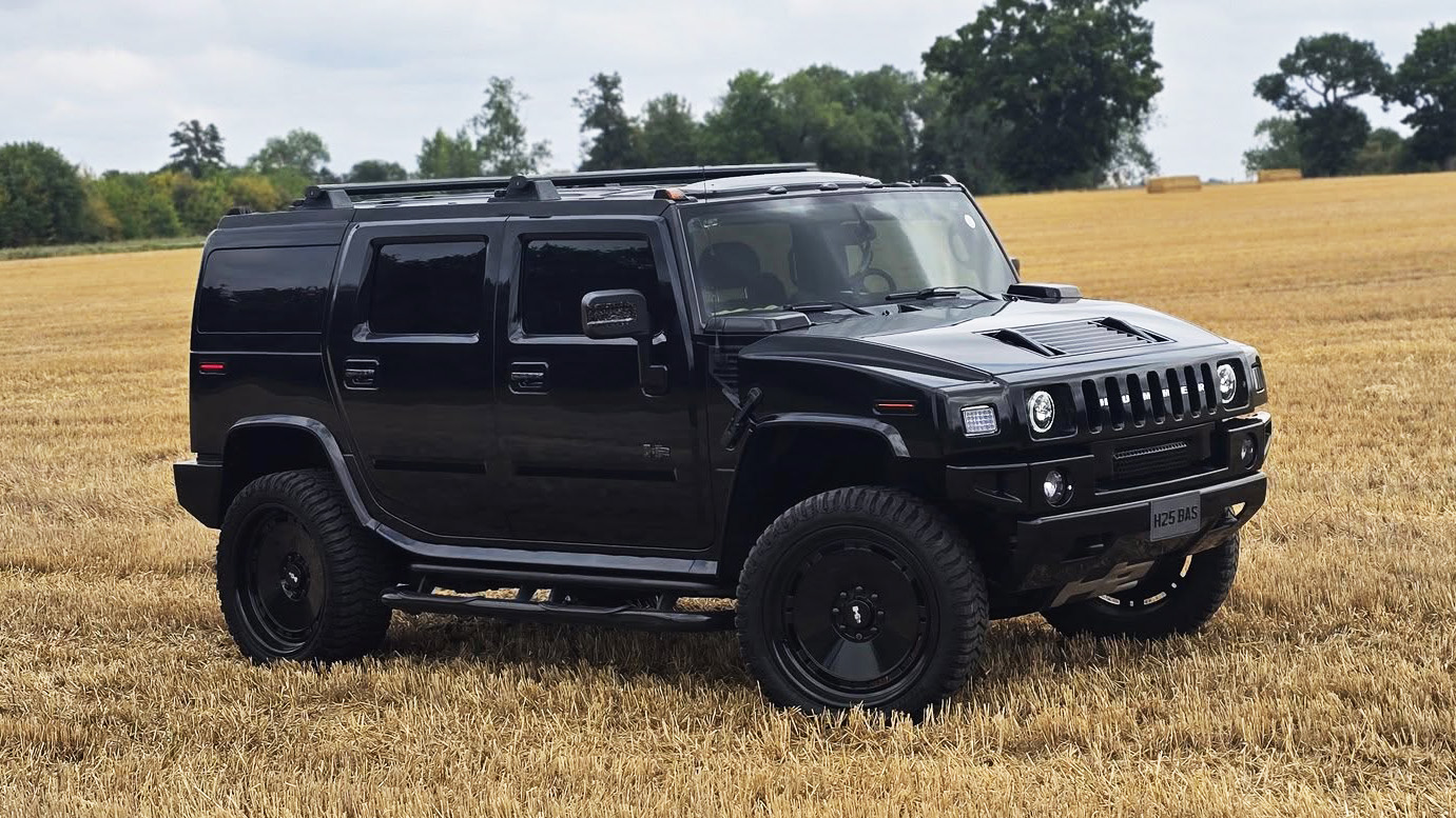 Right side view of black Hummer H2 with privacy tinted windows parked in an open field.