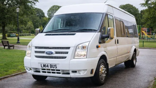 White Ford Mini Bus parked in the middles of a Park with greenery around it