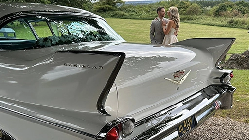 Rear view of an ivory American Cadillac with Bride and Groom standing in the background.