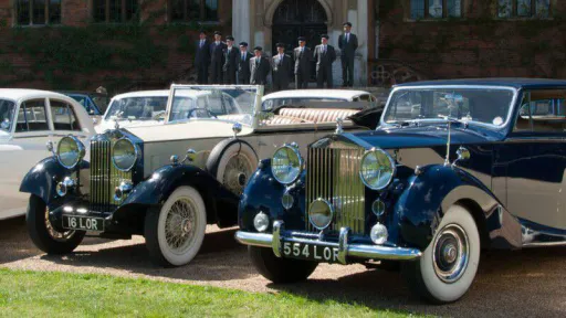 Three Classic and Vintage Cars available in Andover are parked in front of a grand wedding venues with fully uniformed chauffeurs in the far background.