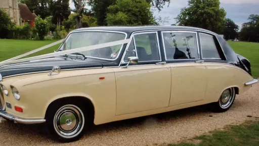 Black and ivory Daimler limousine parked on a gravel driveway, side profile view with green lawn and trees in the background.
