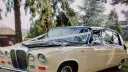 Front three quarter view of a black and ivory Daimler limousine parked under trees, chrome grille and twin headlights clearly visible.