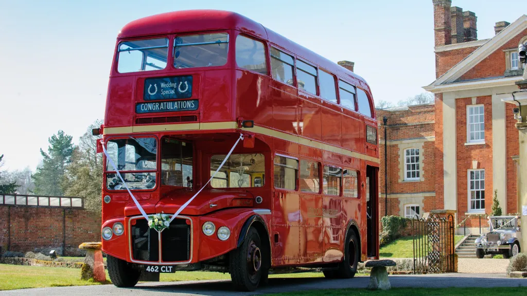 Red vintage Routemaster double decker wedding bus parked outside a country house venue with green lawns.