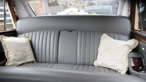 Rear cabin interior of classic Daimler limousine with silver leather bench seating, pleated upholstery and cream cushions.