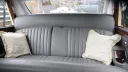 Rear cabin interior of classic Daimler limousine with silver leather bench seating, pleated upholstery and cream cushions.