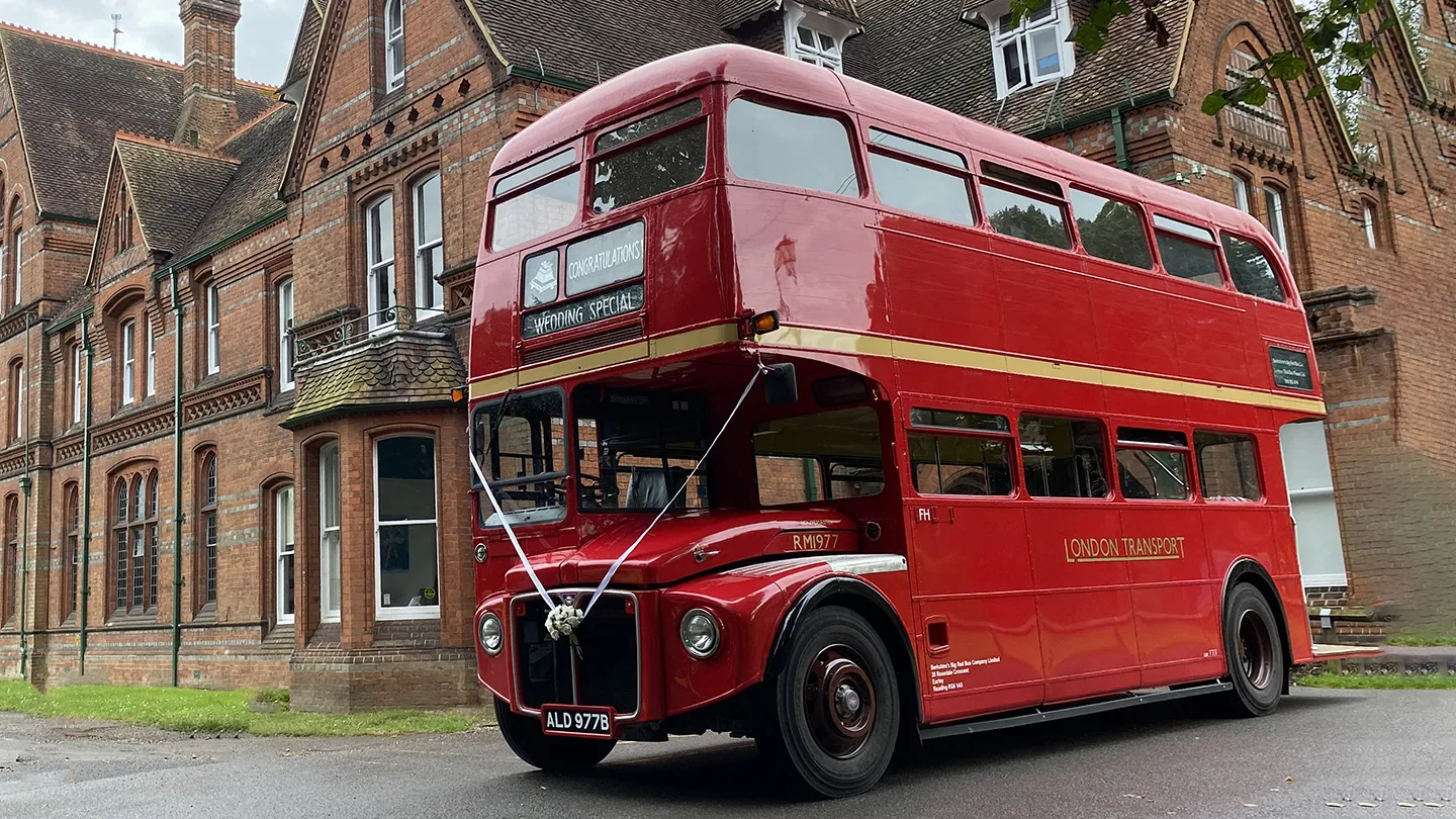 Red vintage Routemaster double decker wedding bus parked outside a historic brick building.
