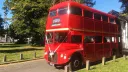 Red AEC Routemaster double decker wedding bus parked on a grass area beside a country wedding venue with trees and blue sky.