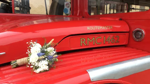 White bridal bouquet resting on the rear engine cover of a red Routemaster double decker wedding bus.