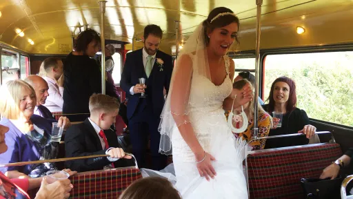 Bride walking down the aisle inside a vintage Routemaster double decker bus with seated wedding guests.