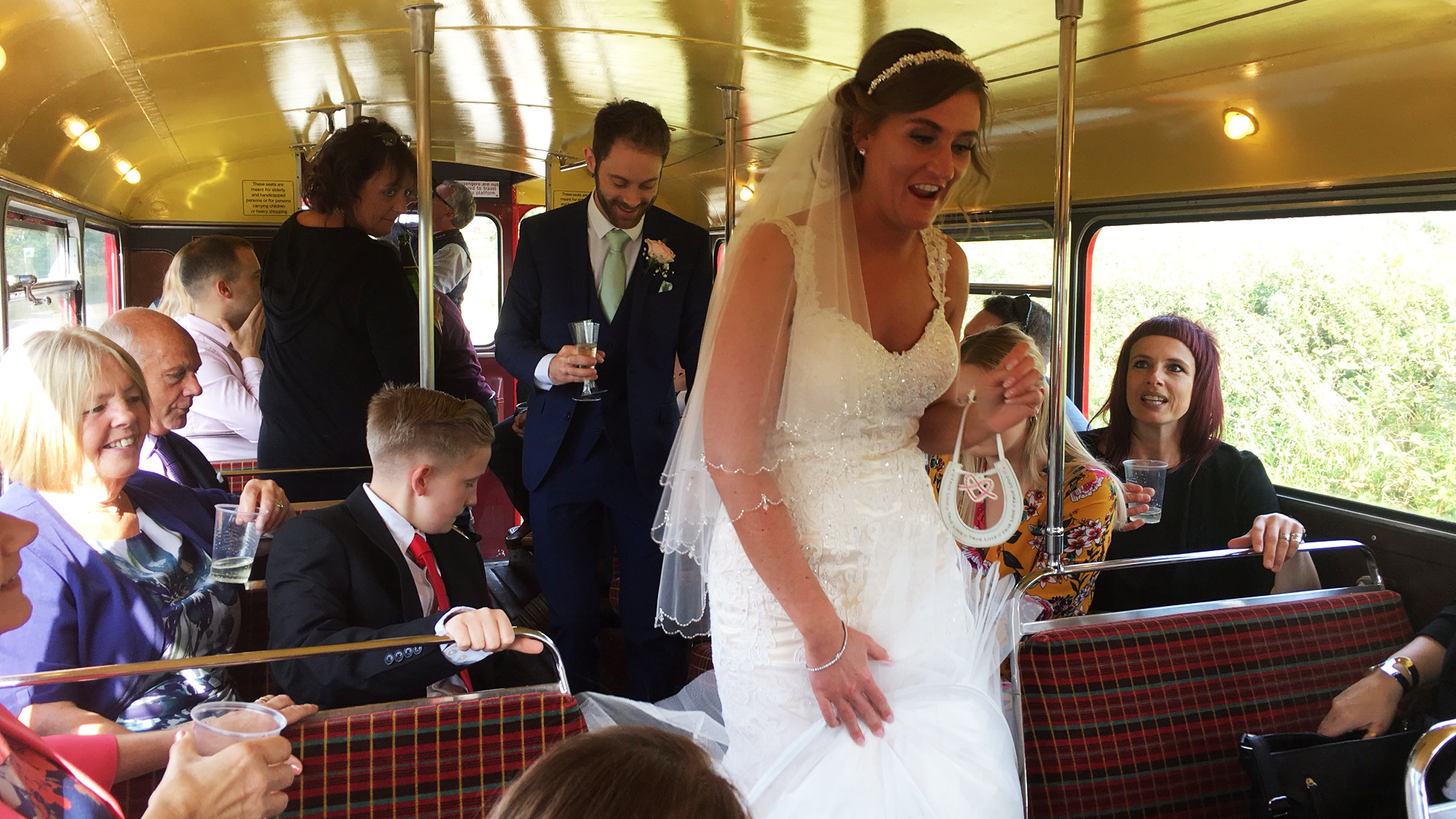 Bride walking down the aisle inside a vintage Routemaster double decker bus with seated wedding guests.