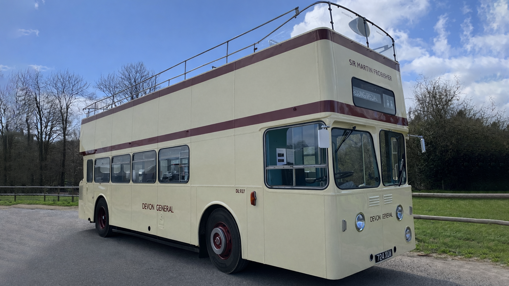 Cream vintage Leyland double decker bus parked on a country road with fields and trees in the background.