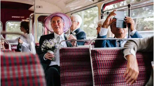 Wedding guests seated inside a vintage red Routemaster bus with tartan seats and champagne glasses.