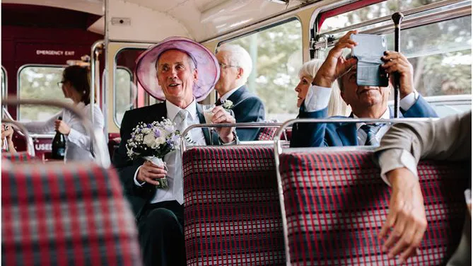 Wedding guests seated inside a vintage red Routemaster bus with tartan seats and champagne glasses.