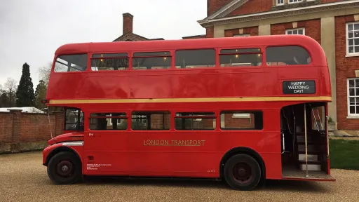 Left side view of a red Routemaster double decker bus showing the open rear platform parked beside a wedding venue.