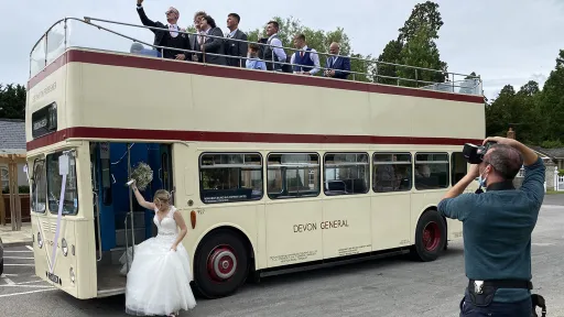 Cream open top Leyland double decker wedding bus with passengers seated on the upper deck during a wedding event.