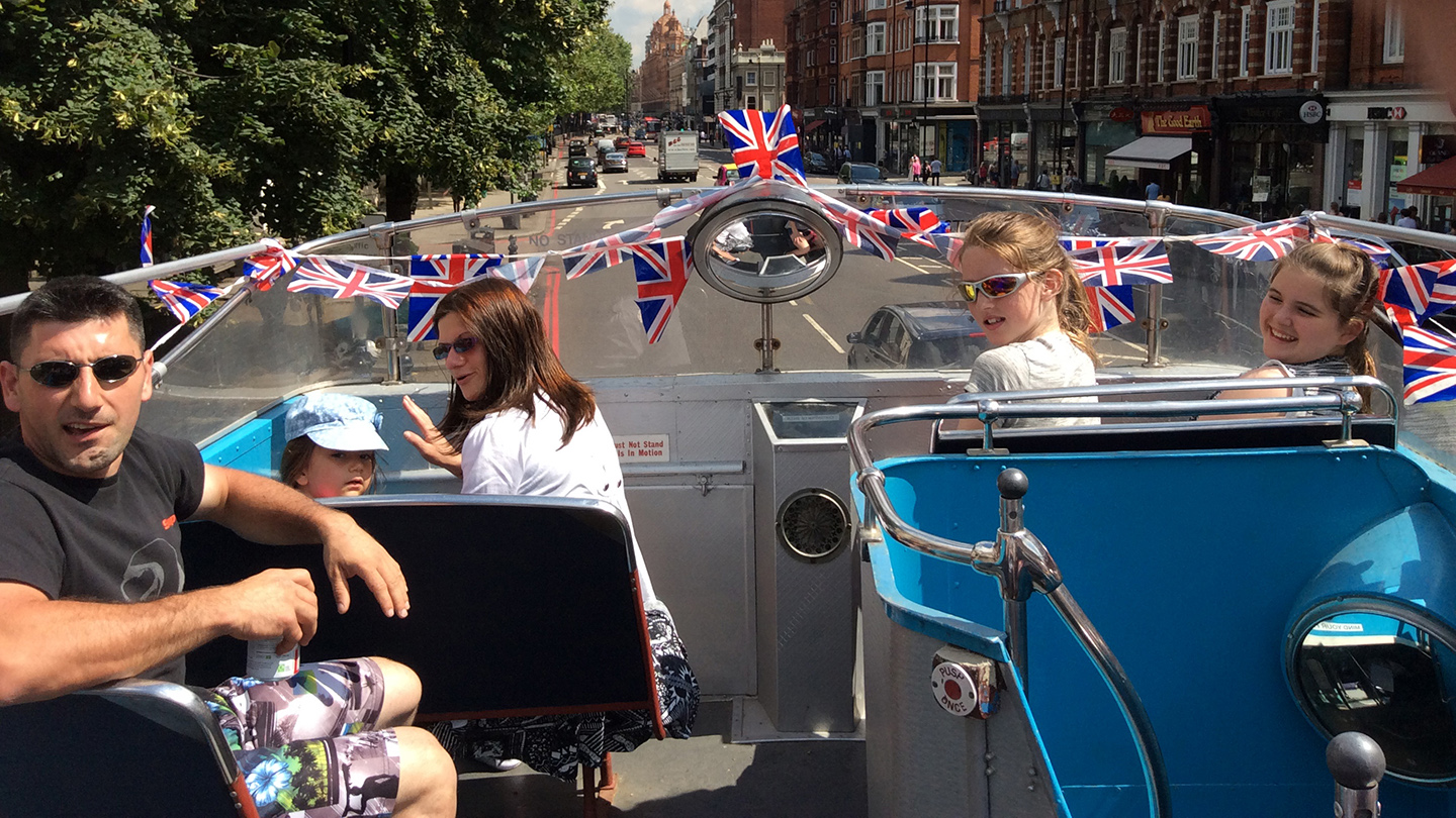 Wedding guests enjoying the view while seated on the open top upper deck of a cream Leyland double decker bus.
