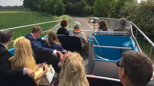 Passengers seated on the open top deck of a cream Leyland vintage bus travelling through the countryside.