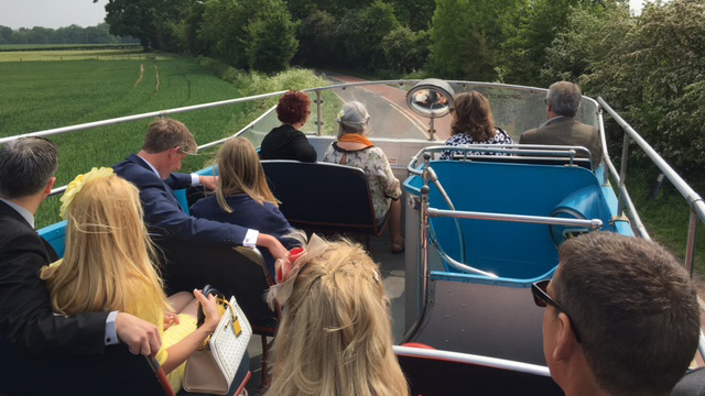 Passengers seated on the open top deck of a cream Leyland vintage bus travelling through the countryside.
