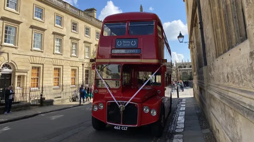 Red Routemaster double decker wedding bus decorated with white ribbons driving through a historic street in Reading.