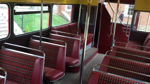 Interior seating area of a vintage Routemaster bus showing classic patterned bench seats and handrails.