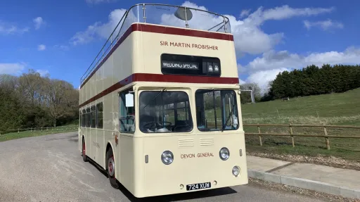 Front view of a cream open top Leyland double decker wedding bus parked beside countryside fields.