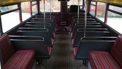 Upper deck interior of a vintage Routemaster bus with rows of classic seats and large windows.