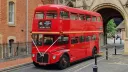 Red Routemaster double decker wedding bus parked beside a historic city building.