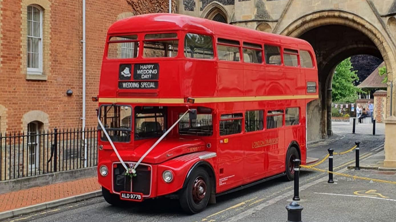 Red Routemaster double decker wedding bus parked beside a historic city building.