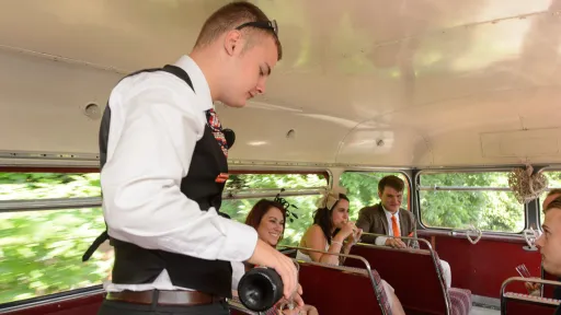 Waiter serving champagne to wedding guests inside a red Routemaster double decker wedding bus.