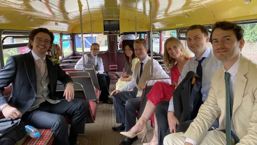 Wedding guests seated inside a vintage red Routemaster bus smiling during transport between venues.