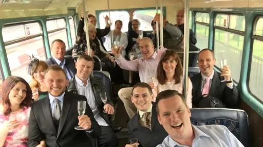 Wedding guests smiling and seated inside the lower deck of a vintage cream Leyland double decker bus.